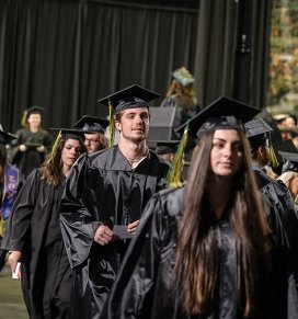 Graduates walk out of commencement, holding their diplomas