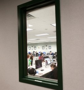 Students are seen through the window of an on-campus computer lab
