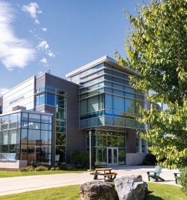 Image of Adirondack Hall in the summer with a blue sky and picnic table in the foreground