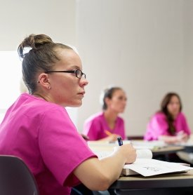 Image of students in pink health care scrubs learning about being personal care aides