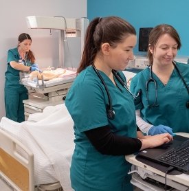 Three nursing students in green scrubs working in a hospital simulation lab