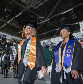 Two graduates march into graduation, smiling