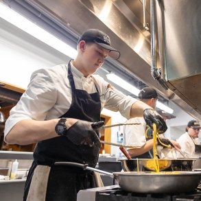 A culinary student tosses pasta in a large pot on a stovetop
