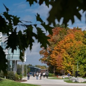 Foliage surrounds a view of students walking across campus on a sunny, blue-sky fall day