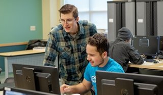 An instructor and student discuss over a computer in a lab