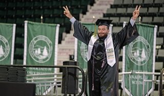 A graduate celebrates as he walks across the stage at commencement