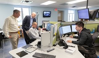 A group of people look over a man's shoulder at a computer screen