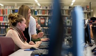 A student and staff member look at a file on a computer