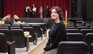 Mary Pilot of Hoosick Falls poses for a photo in the theater, while the cast of "The Addams Family" rehearses in the background.