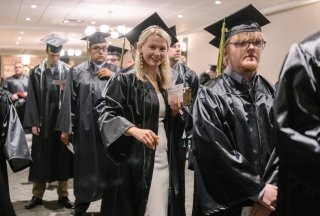 A graduate smiles at the camera as she walks into commencement.