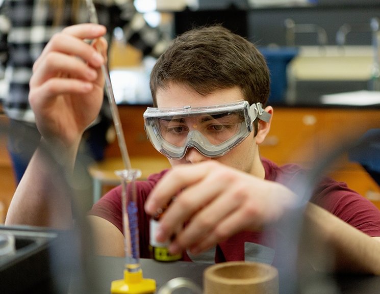 A student concentrates on a vial in a science laboratory