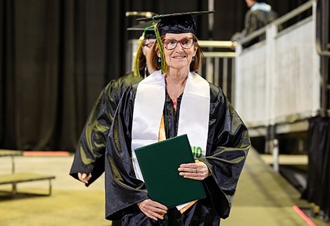 A graduate smiles as she holds her degree tight to her chest at the 2025 commencement ceremony
