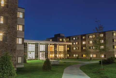 Image of the residence hall in the evening with a dark blue sky and all of the lights on