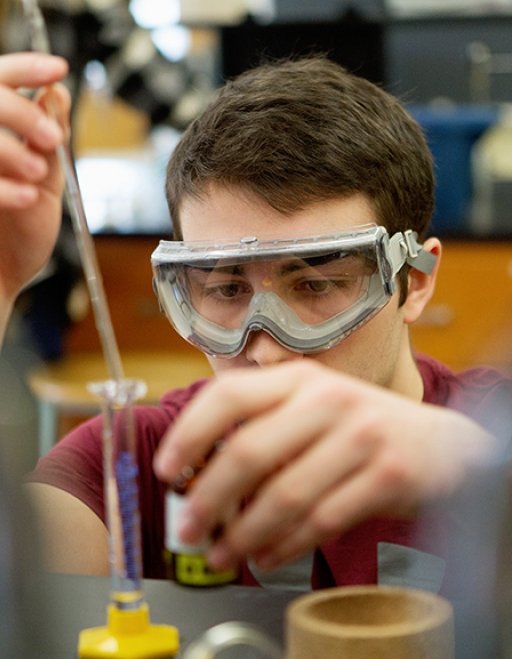 A student concentrates on a vial in a science laboratory